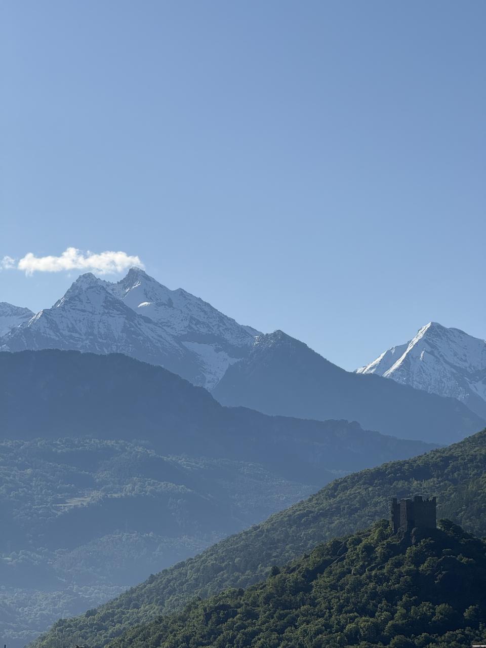 des montagnes en arrière plan et au milieu un mont de forêt moins haut avec un château médiéval en contre jour