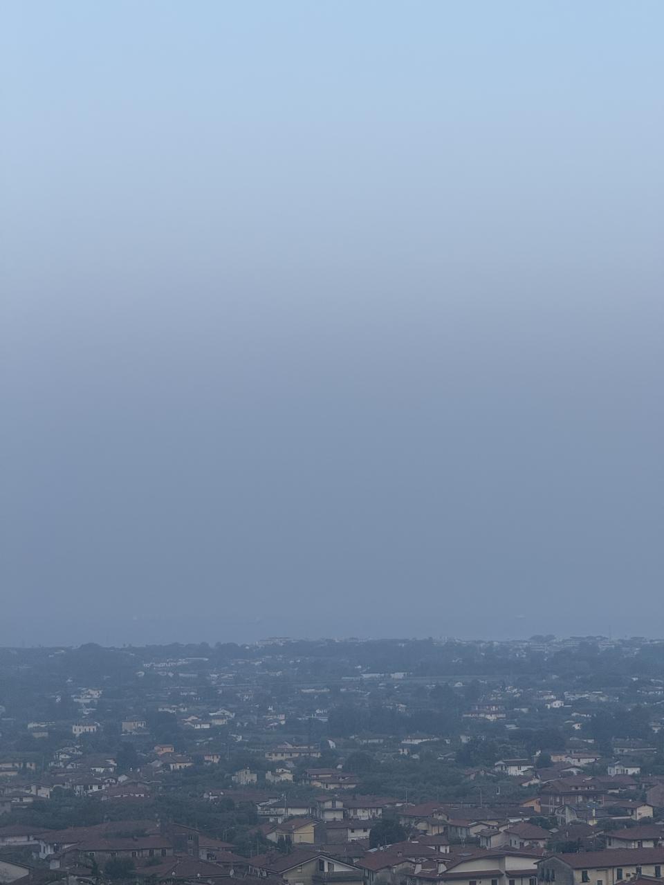 une ville au premier plan puis un ciel qui devrait laisser voir la mer mais on voit plutôt un nuage de pollution 