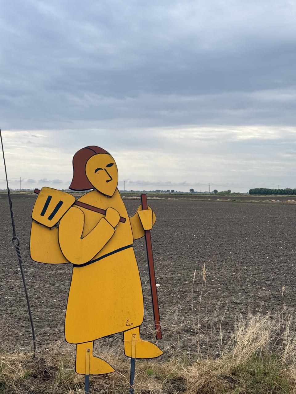 un personnage en bois orange qui est sur le bord du chemin il représente une personne effectuant un pèlerinage