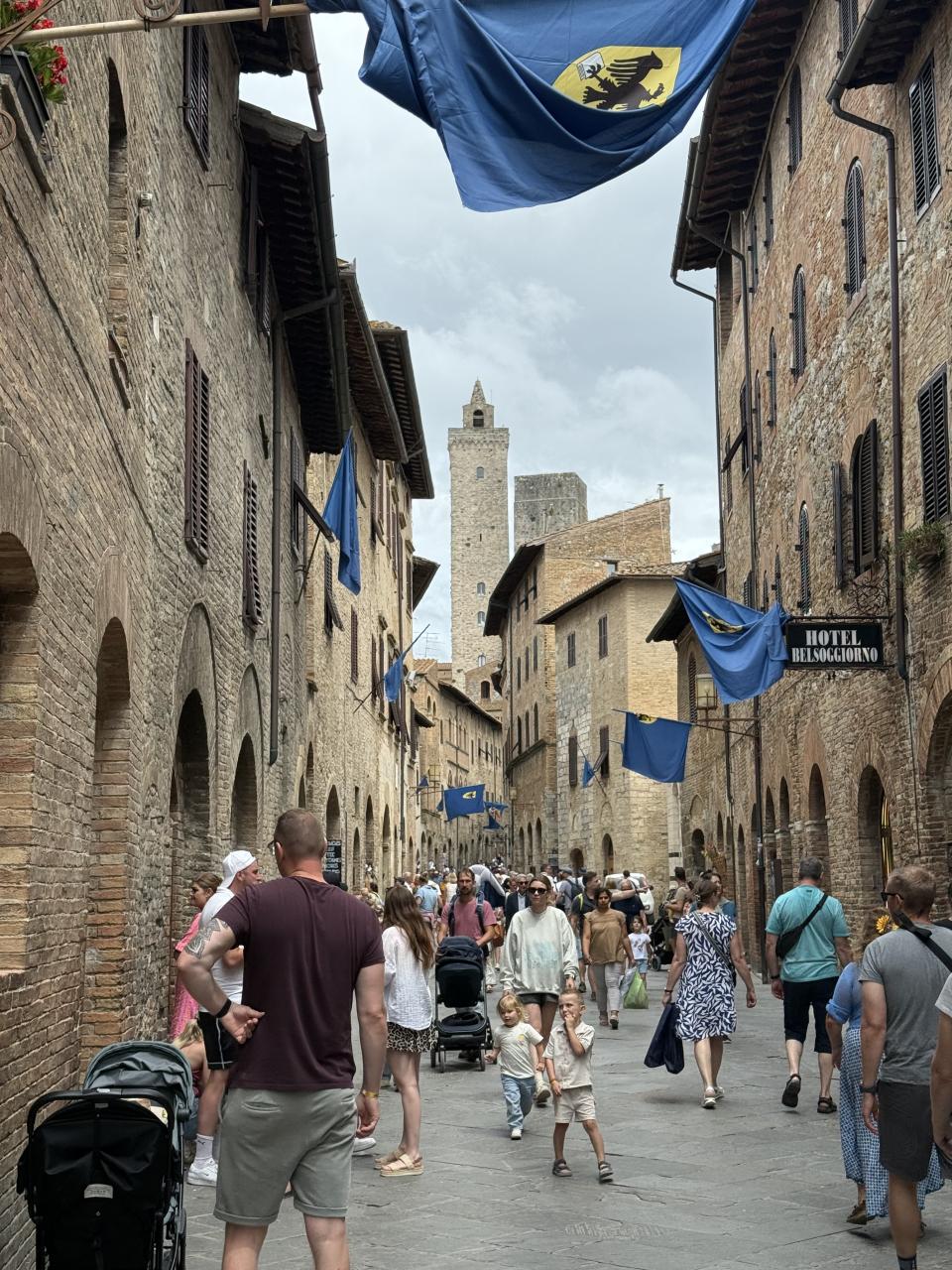 une ruelle fortifiée avec plein de gens. On voit des bannières bleu accrochées aux murs