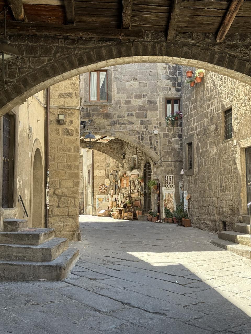 une ruelle pavé qui passe sous un pont de pierre. Le tout est entouré de murs de maisons